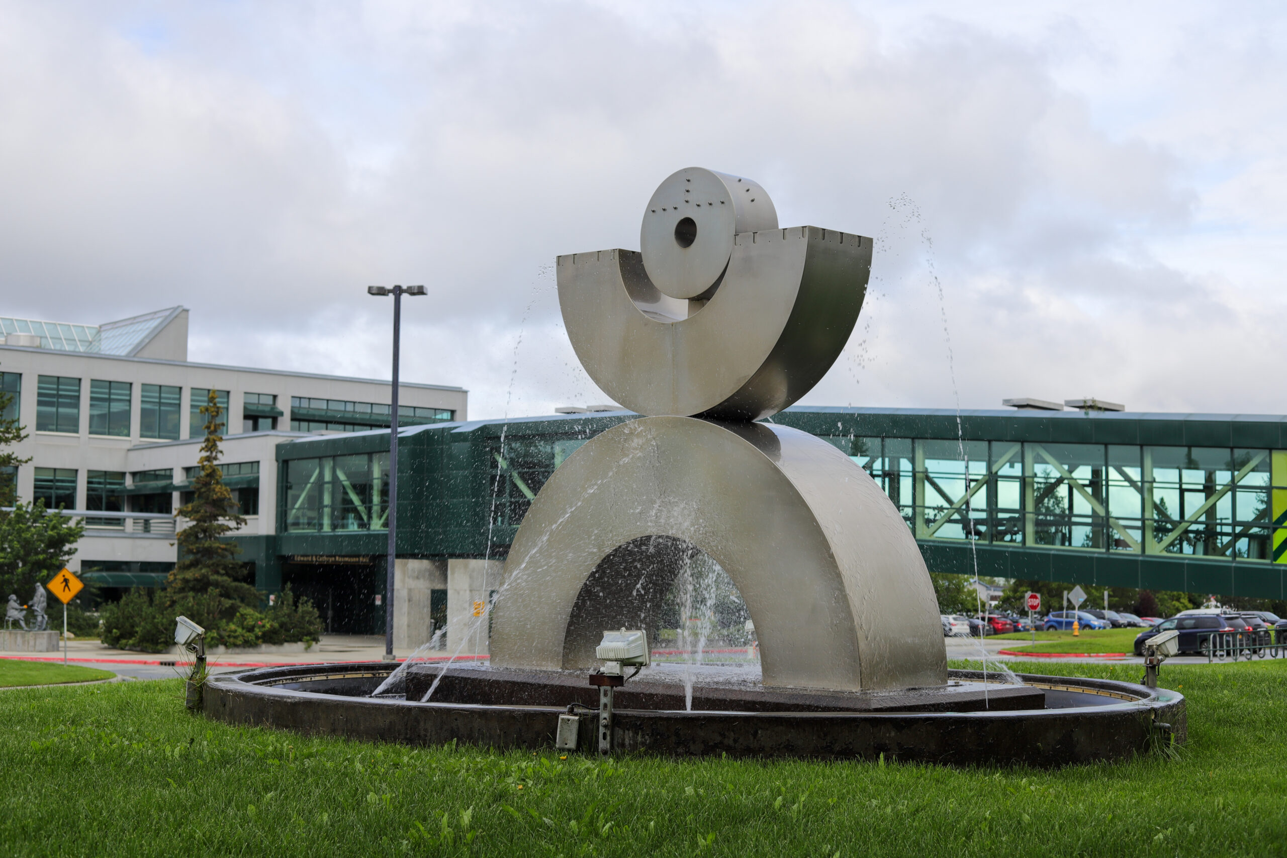 A sculpture / fountain, with an elevated walkway visible behind it.
