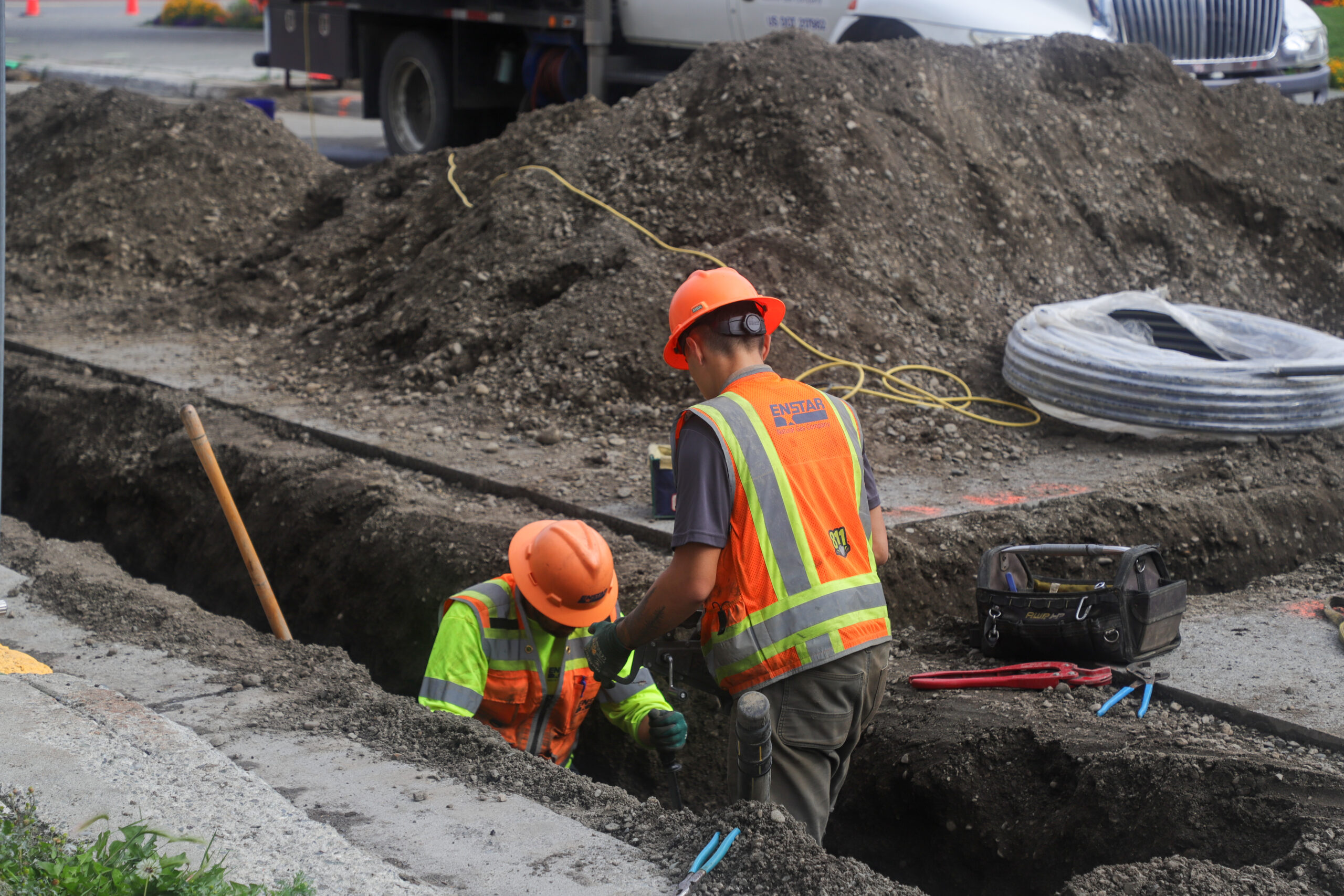 Two people in hardhats and safety vests dig a trench.