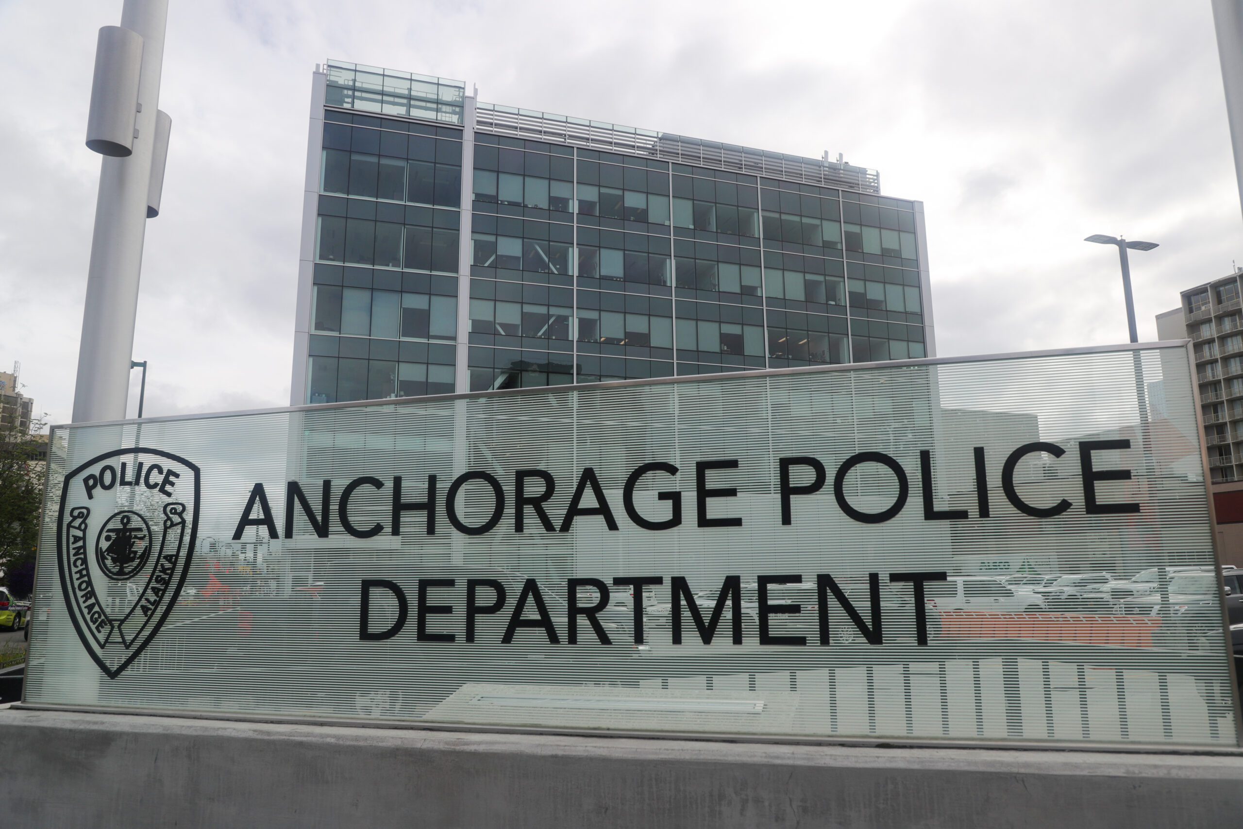 A sign that reads "Anchorage Police Department." There is an office building behind it.