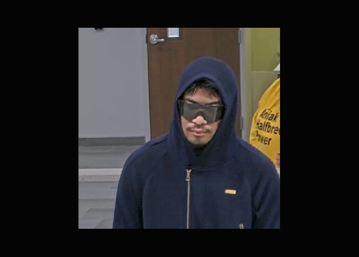 A man wearing a hood and sunglasses, seen in a still from surveillance video