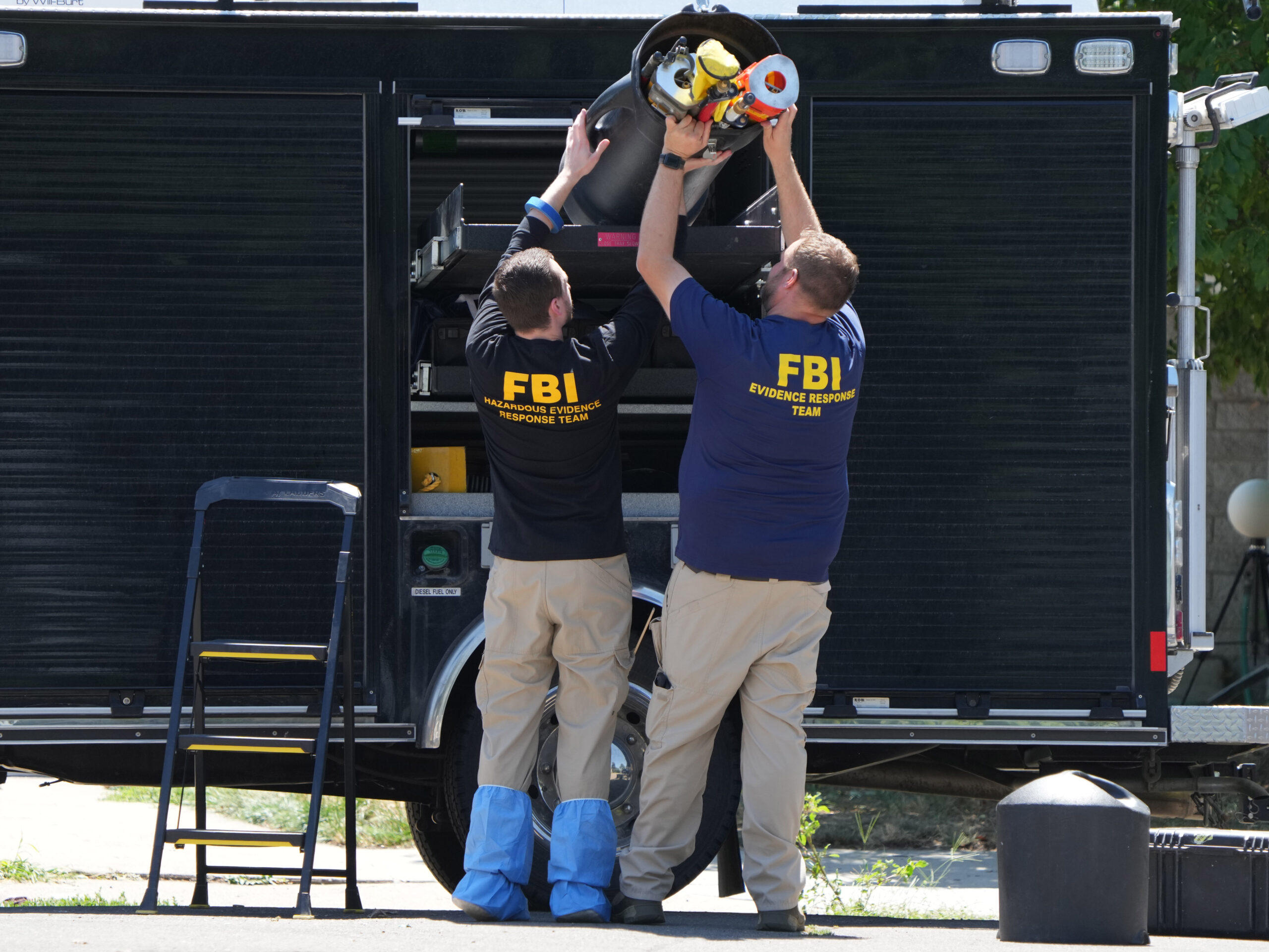 Two people in FBI shirts unload equipment from a truck outside 