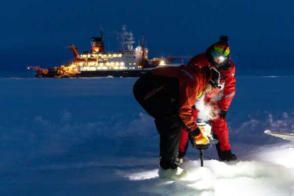 two people drill into sea ice