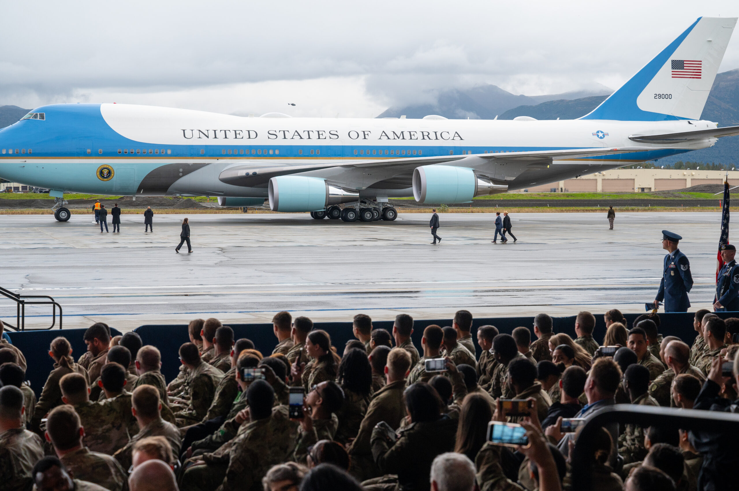 Air Force One on a tarmac as a group of people look on, some taking photos on their cellphones