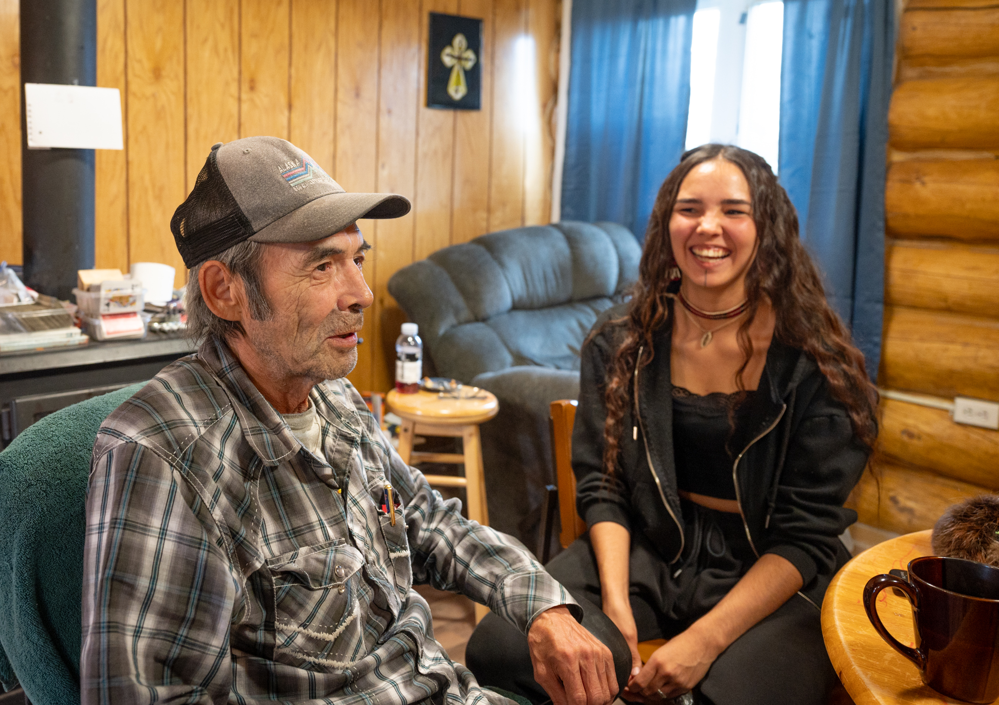 A man and woman share stories by a wood stove.