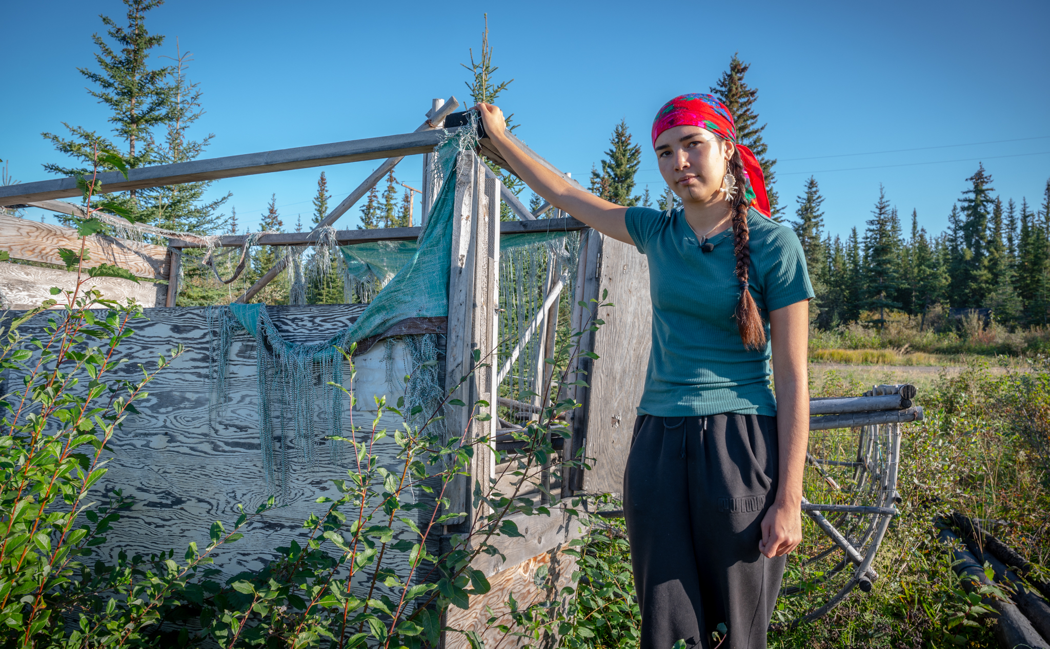 A woman with a red head band on stands by an abandoned fish wheel.