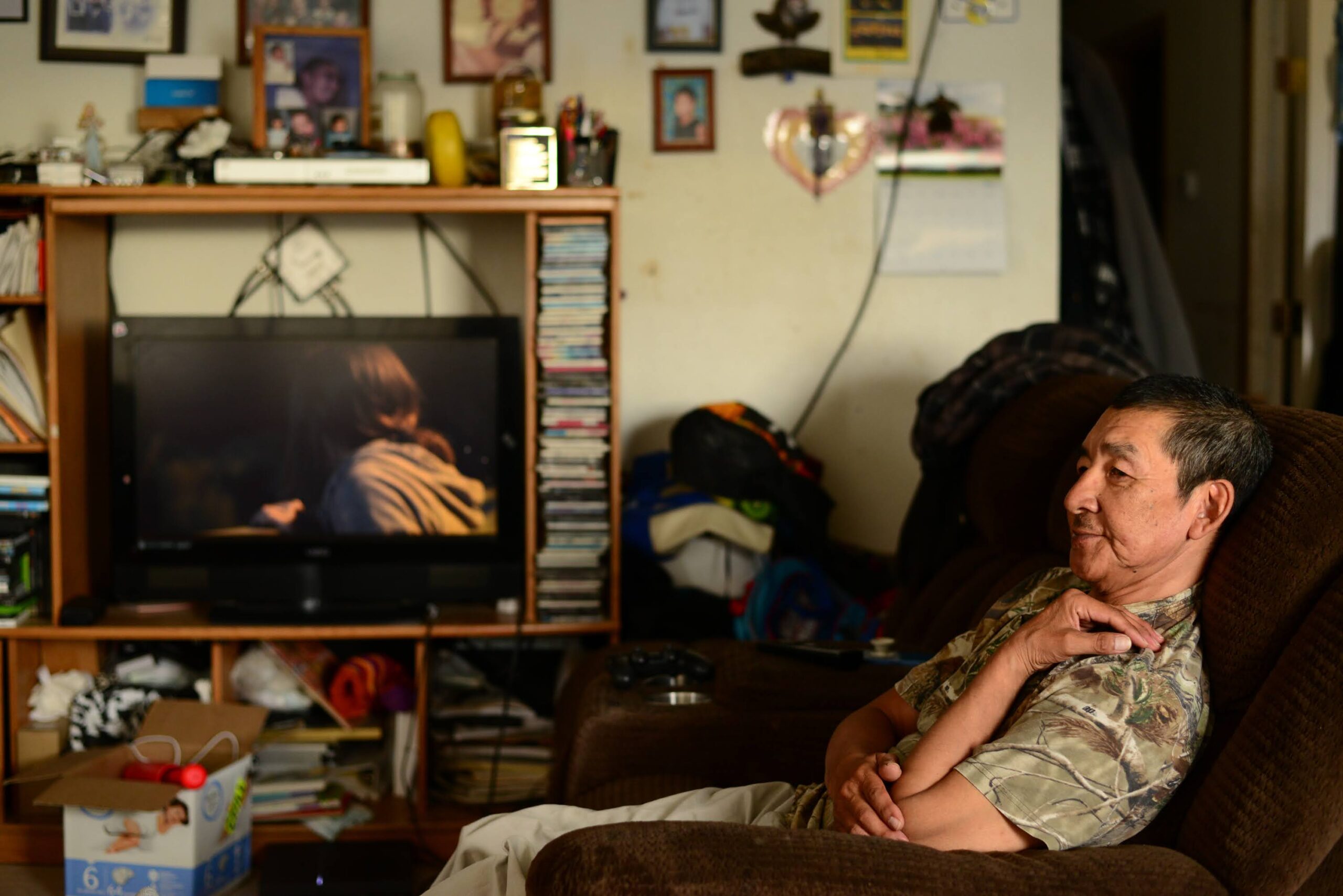 a man sits on a couch inside, with the TV on in the background