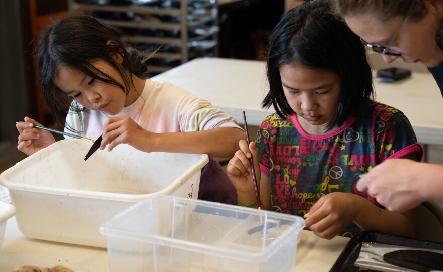 two children learn how to clean artifacts at a table