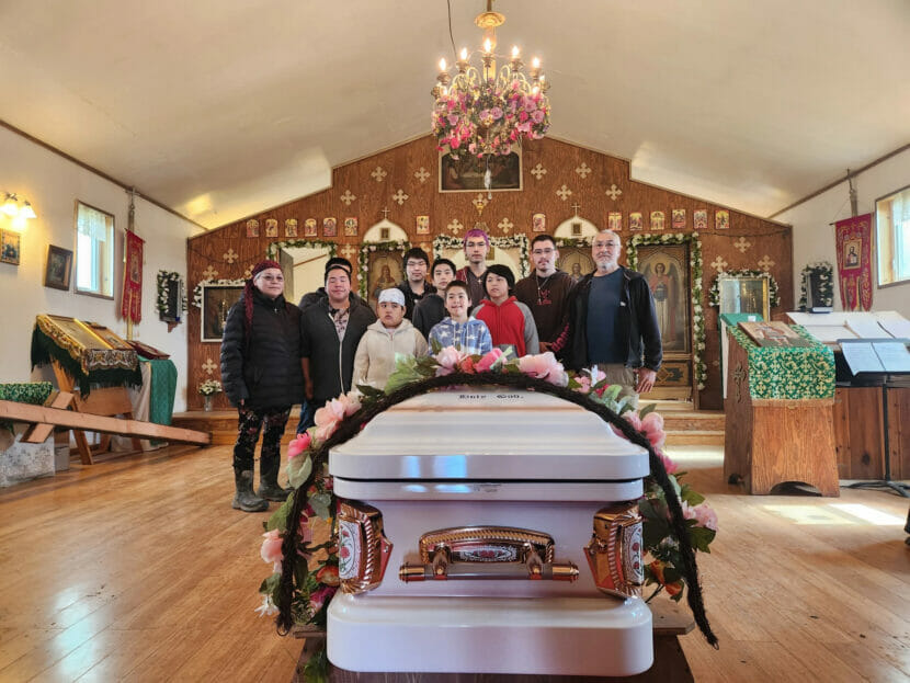 people stand around a casket
