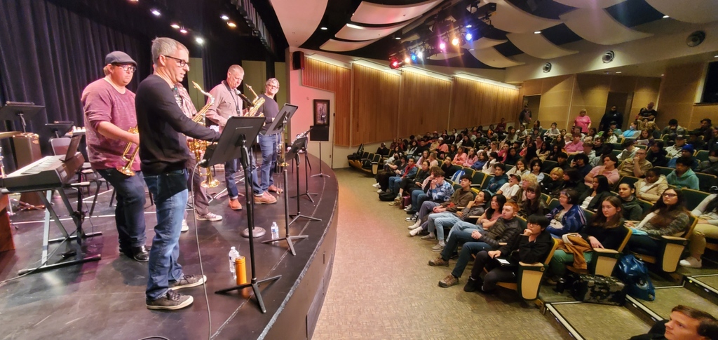 Saxophone and trumpet players play on stage in a high school auditorium. 