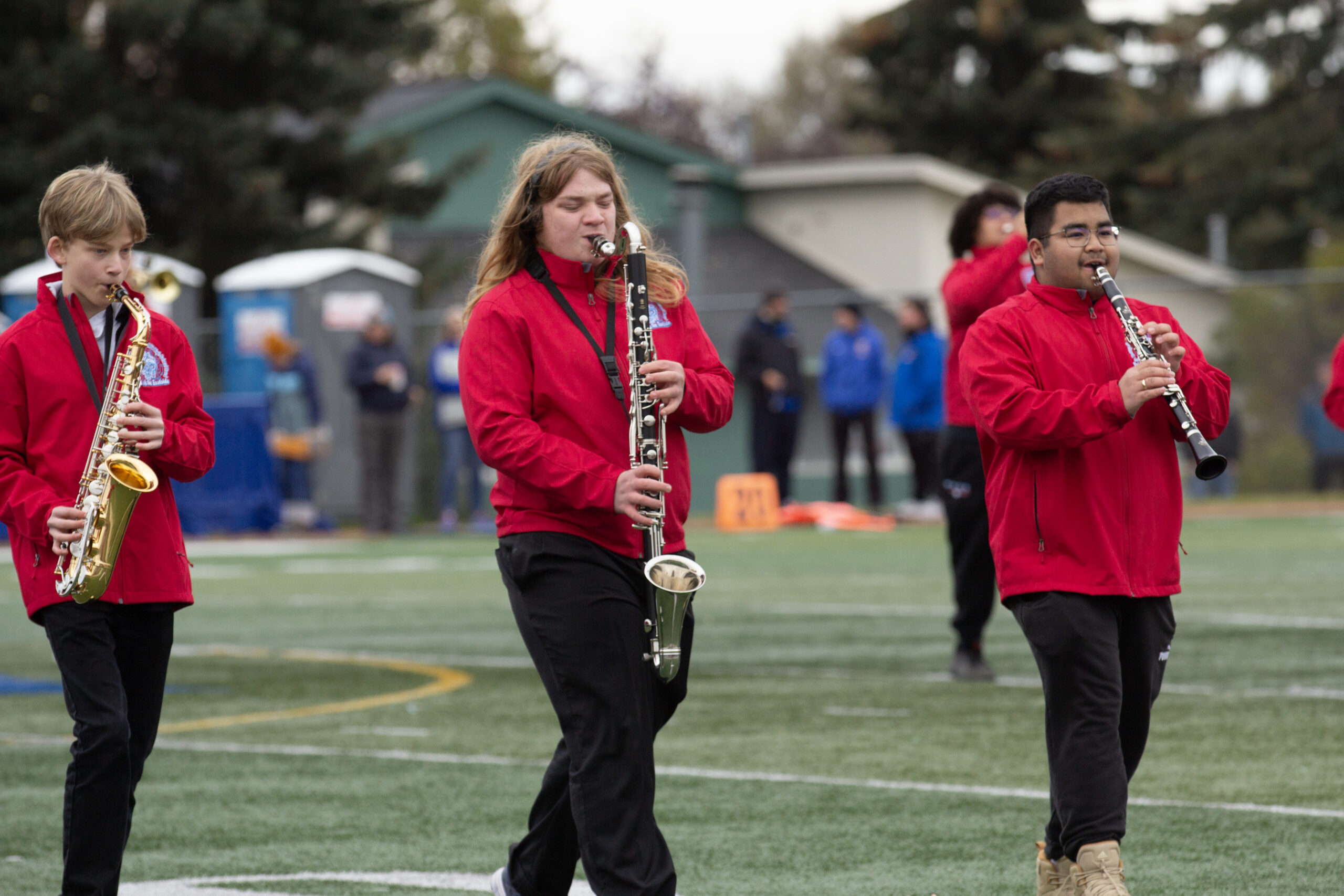 Students in red jackets march and play instruments on a football field (Shiri Segal/Alaska Public Media)