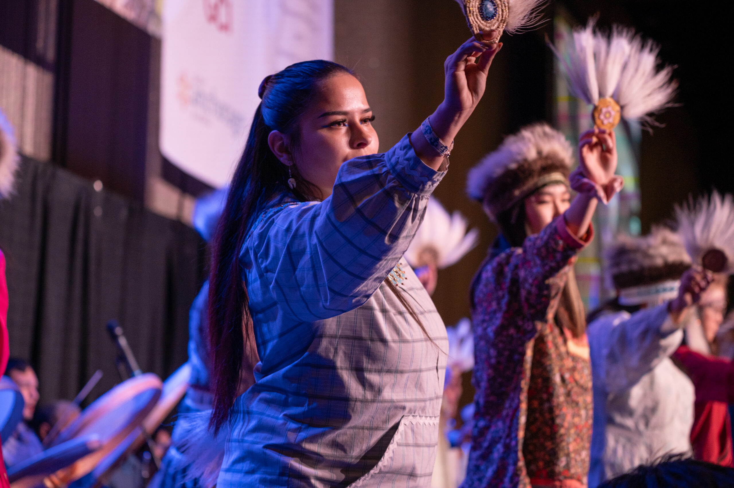 A woman in a kuskpuk waves a native fan in dance.