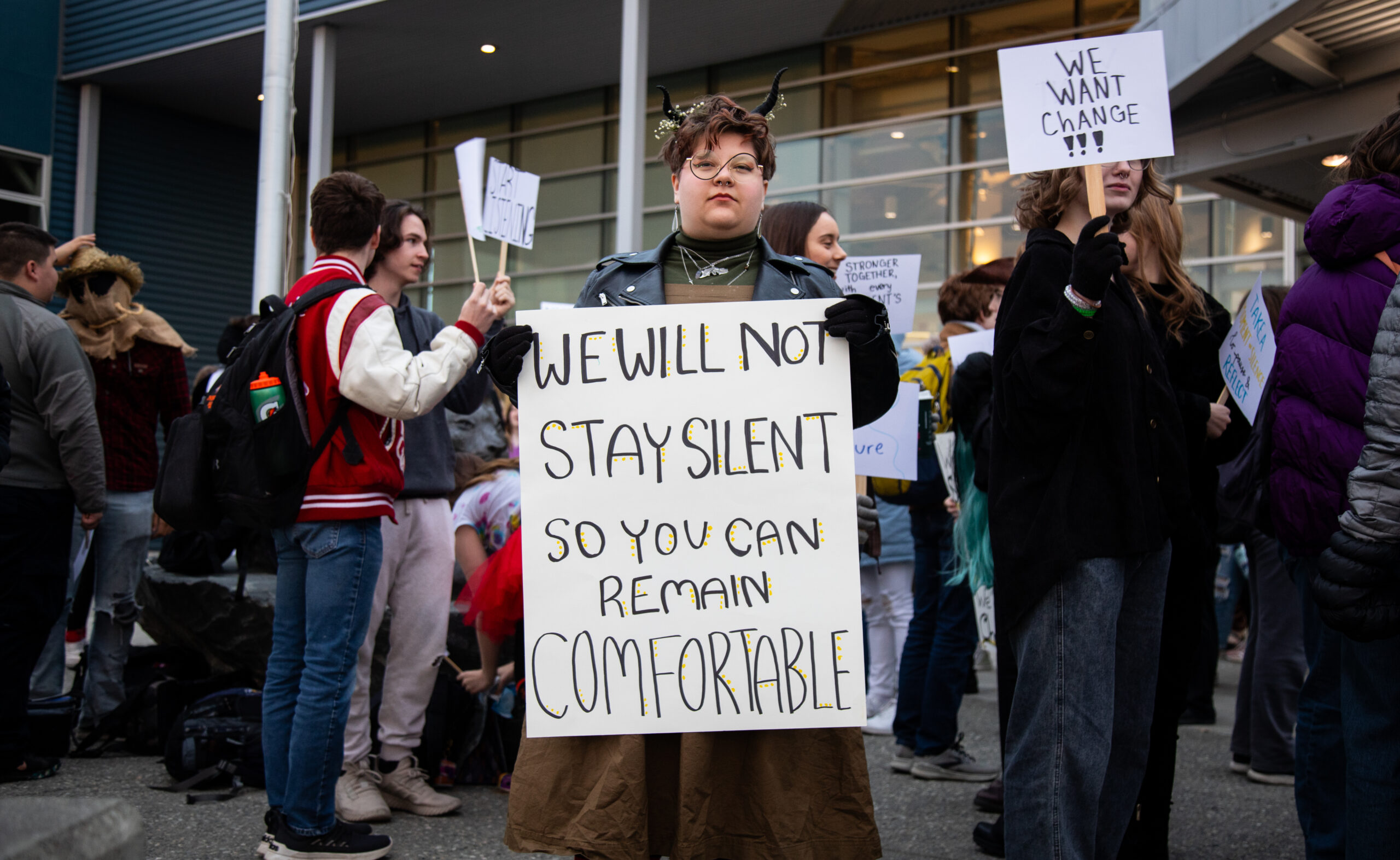 A person in costume stands at a protest with a handmade sign.
