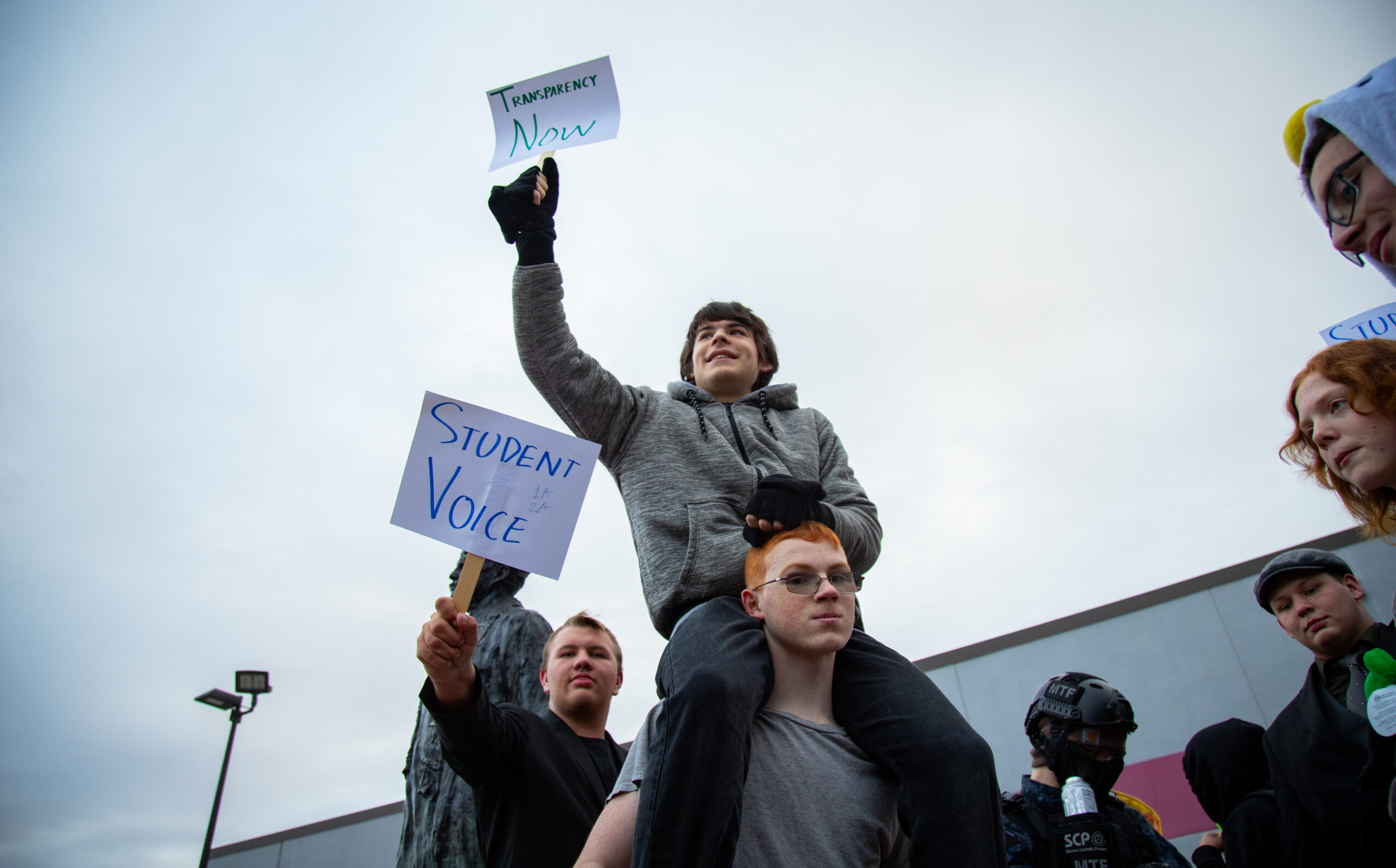 One student holding a sign sits on the shoulders of another student during a walkout to protest recent school board decisions at Wasilla High School.
