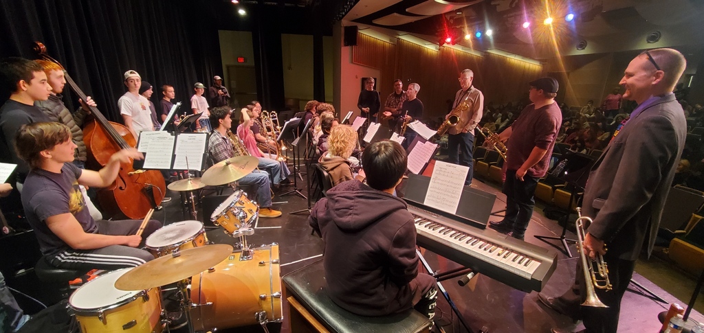 Professional musicians stand on an auditorium stage with a high school jazz band.