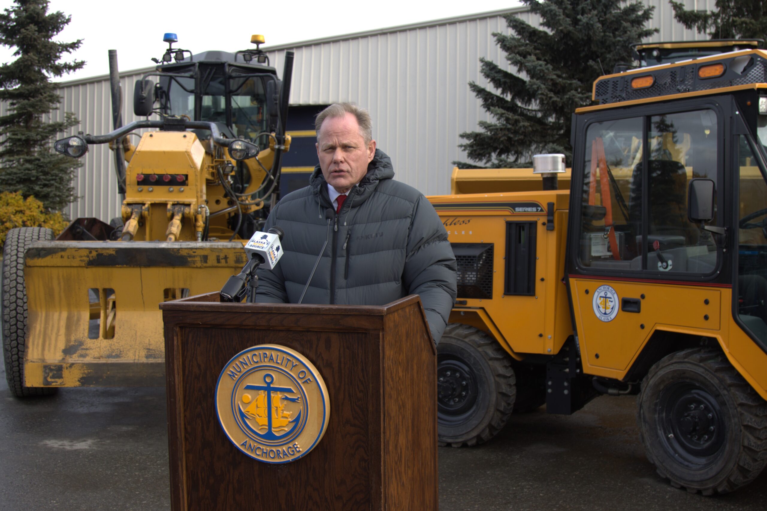 a man speaks from a podium set up by heavy equipment