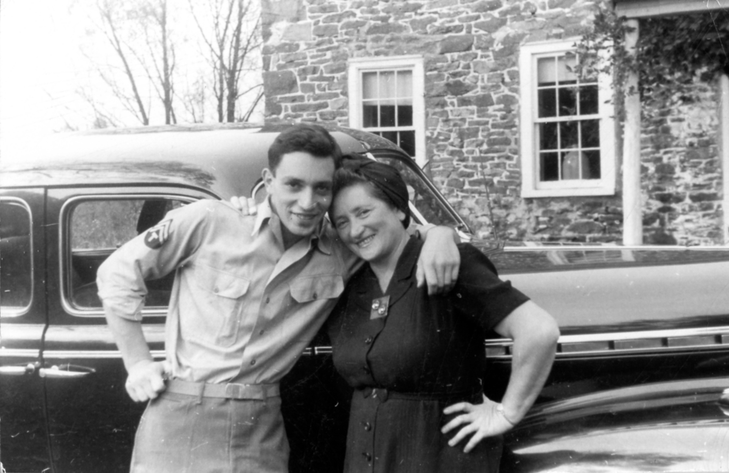 a black and white photo of a mom and her son, posing her a car