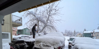 A man shovels snow off his car.