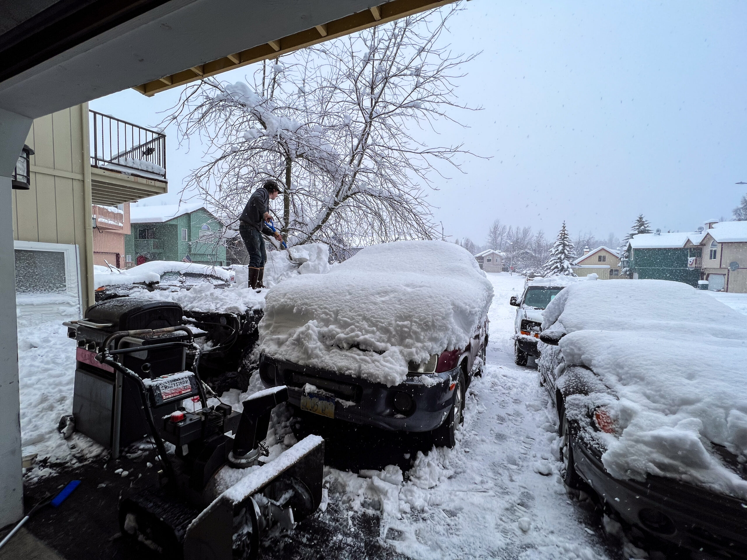 A man shovels snow off his car.