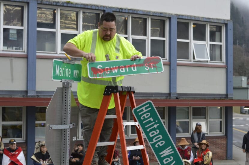 a man on a ladder takes down a street sign that says Seward St crossed out in red