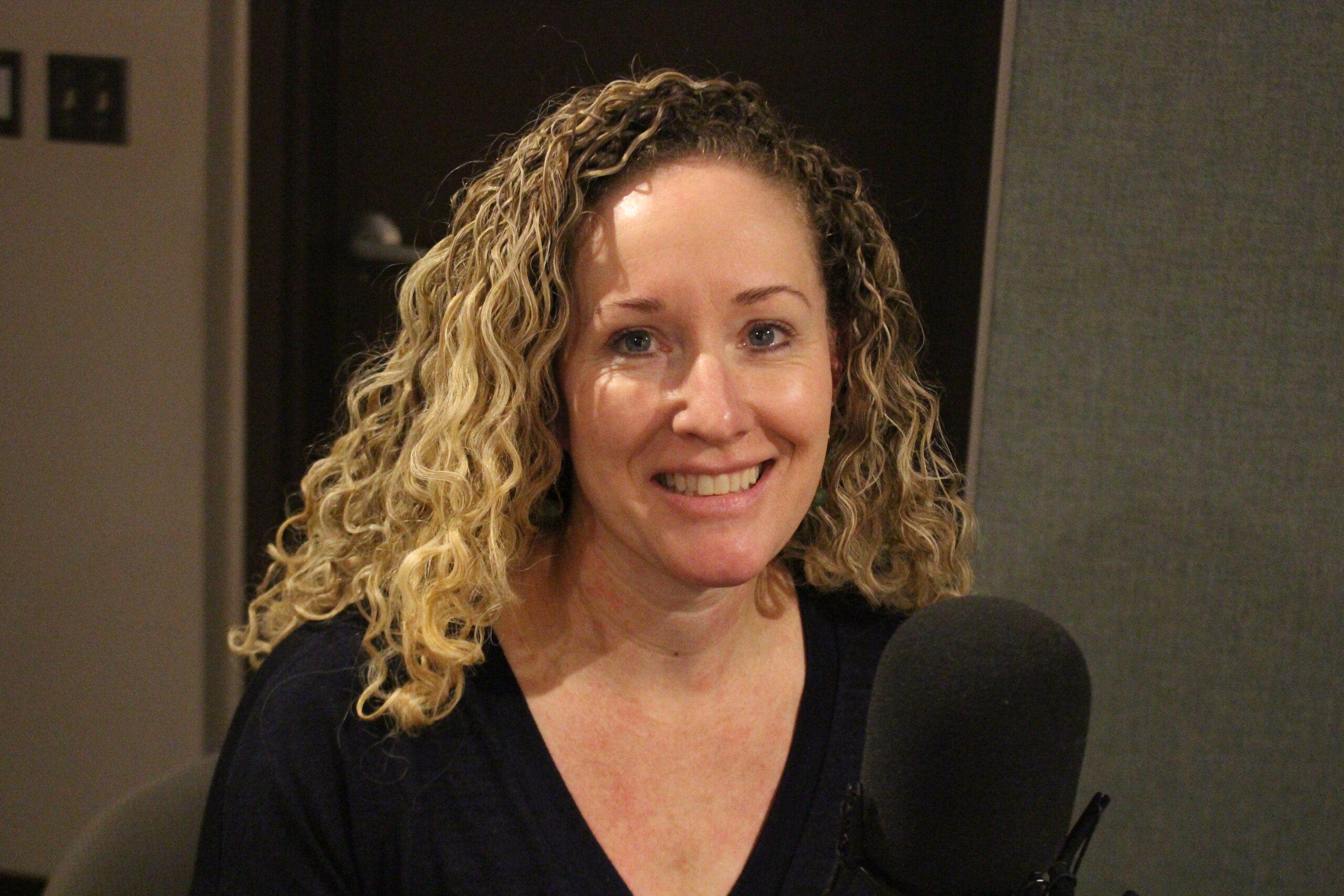 a blonde woman smiles near a microphone