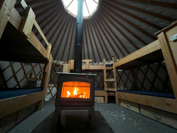 Interior of a yurt with wooden bunk beds and fire in a wood stove. 
