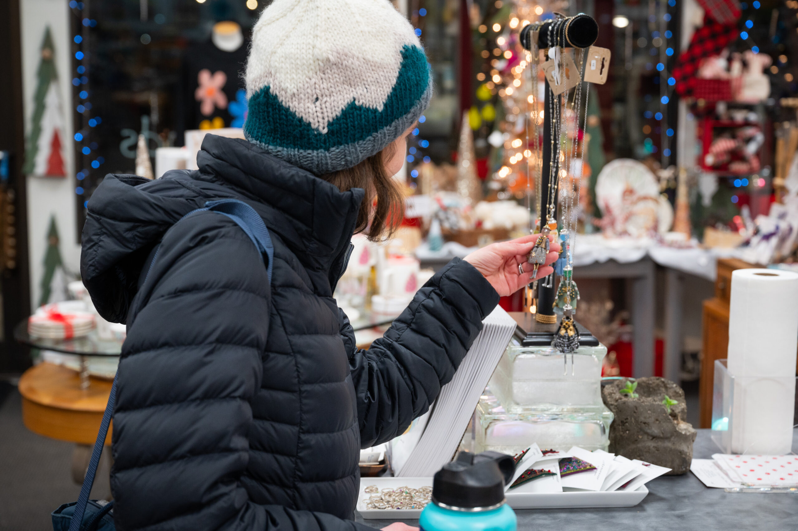 A person wearing a knitted beanie examines jewelery.