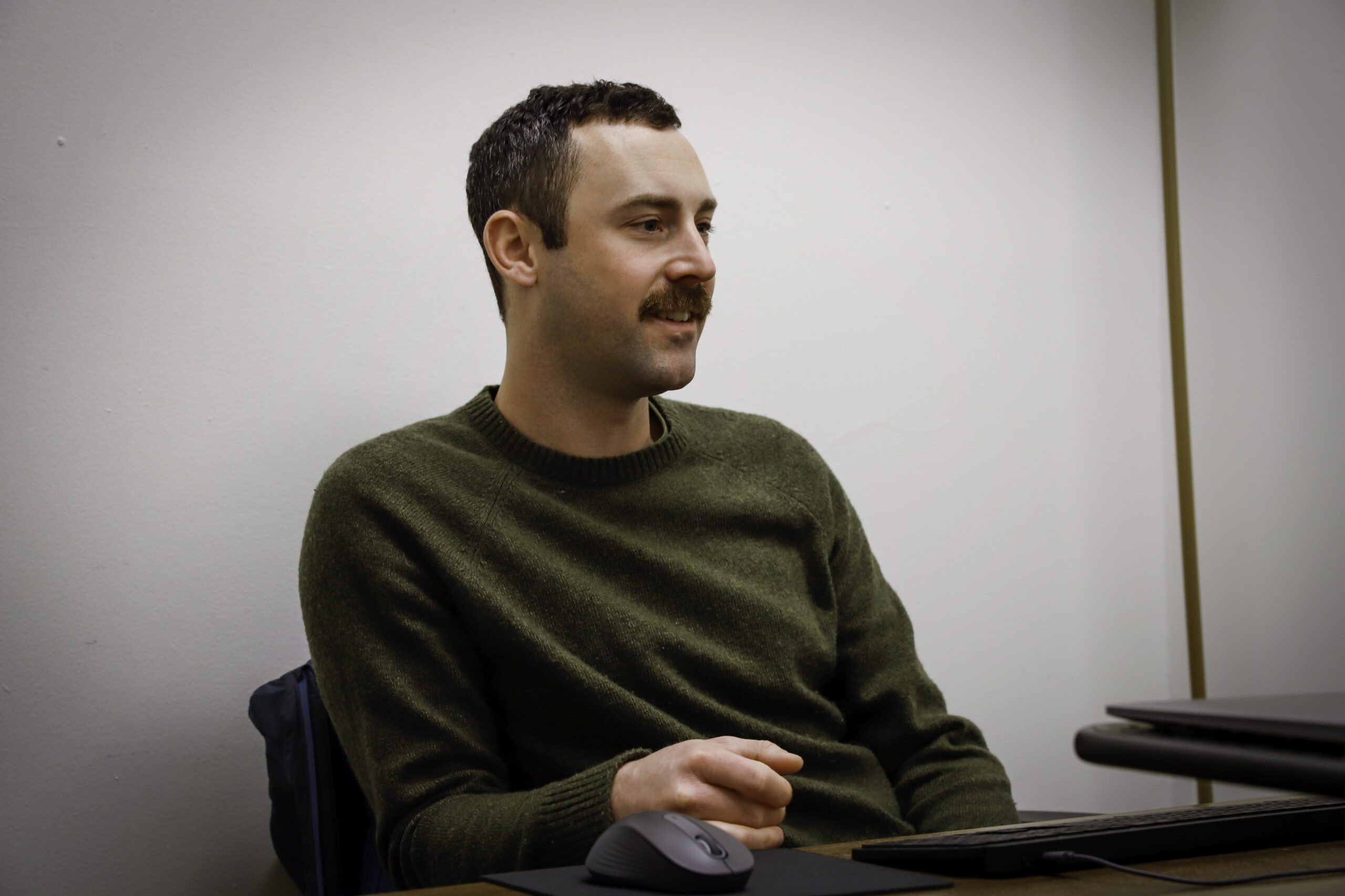 a man with a green sweater sits at a desk