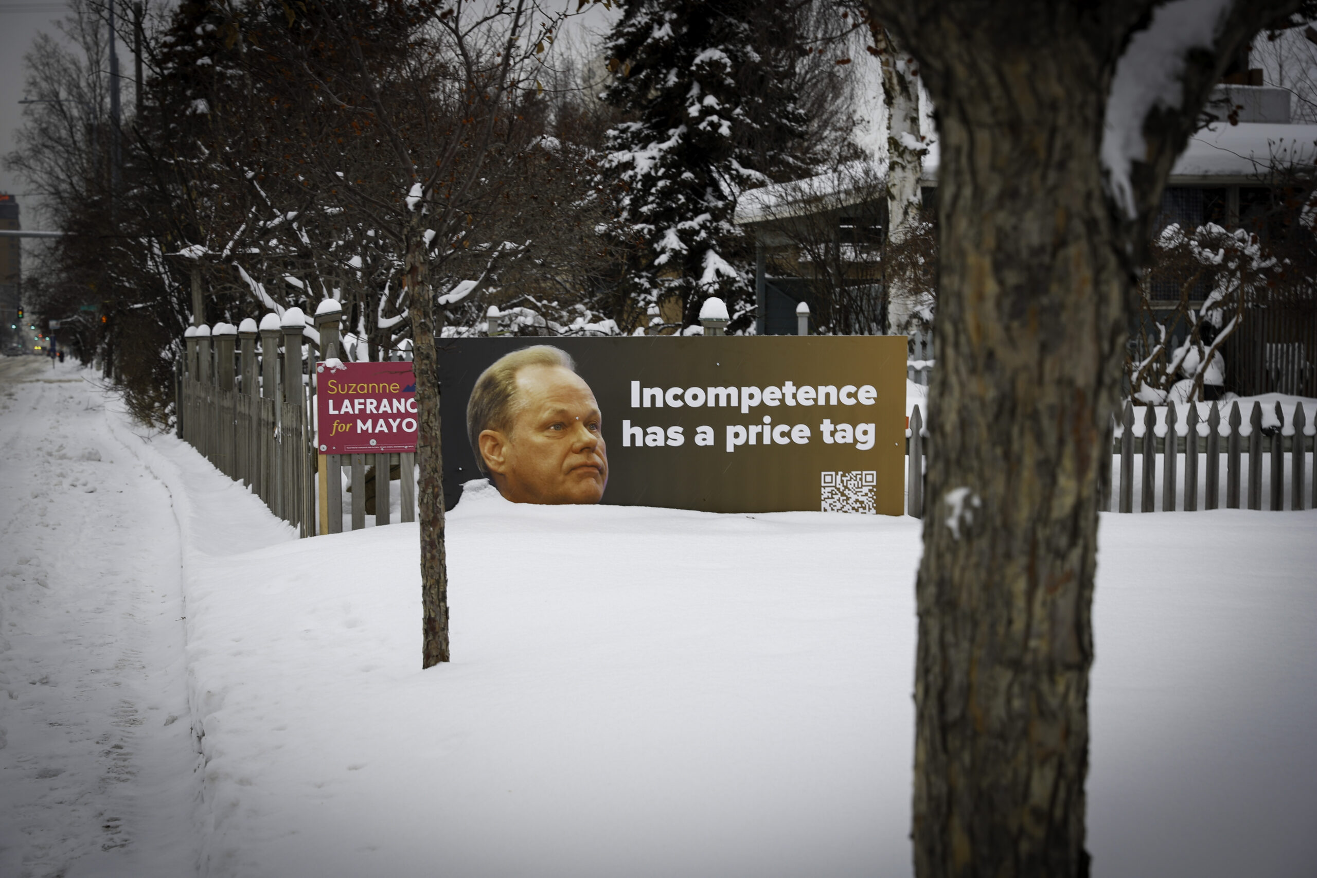 A sign that says, "Incompetence has a price tag" stand halfway buried in snow along a picket fence.