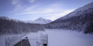 a white, snowy landscape of a dam covered in snow and mountains covered in snow.