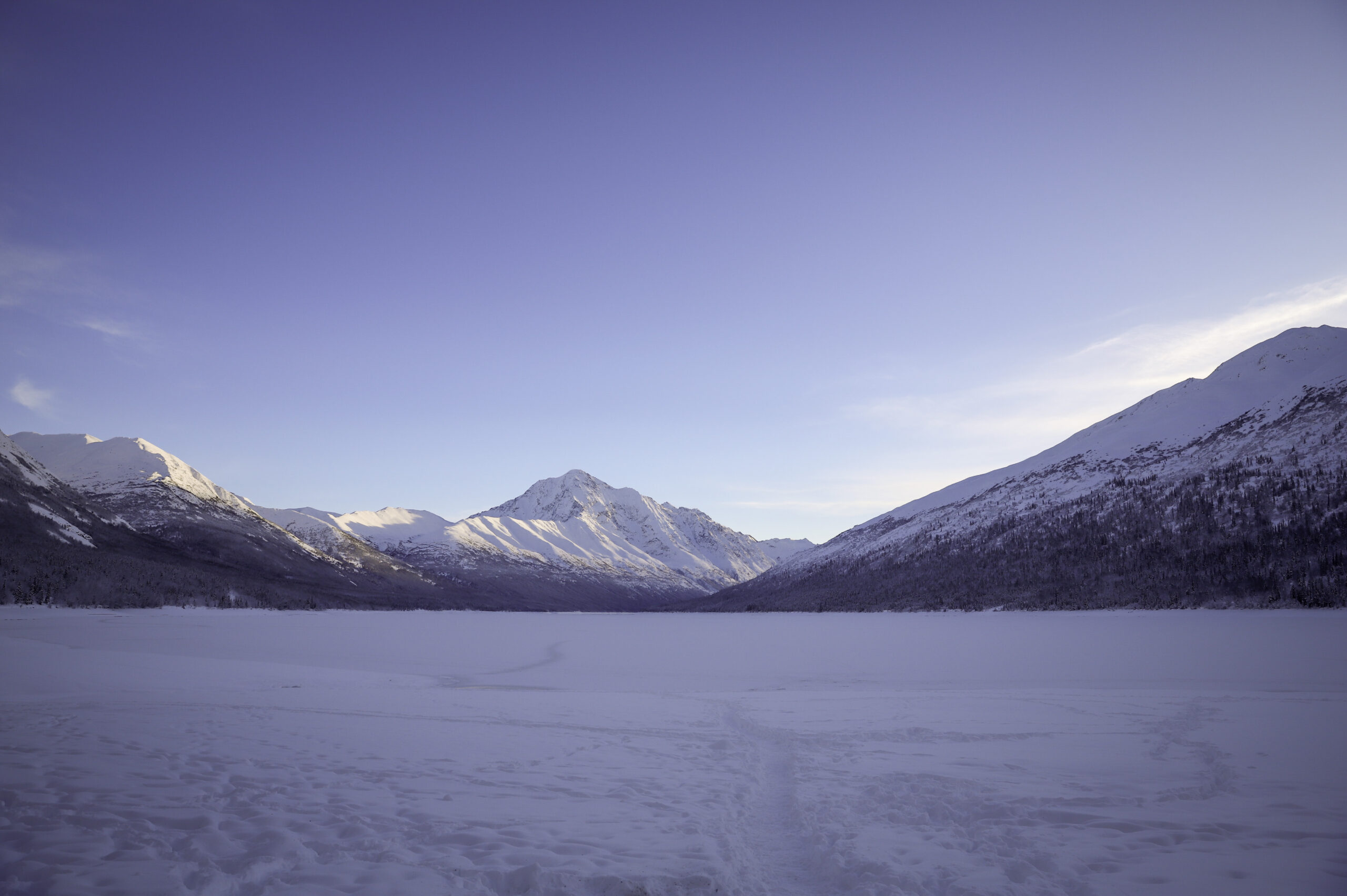 a wide landscape shot of a frozen lake covered in several feet of snow