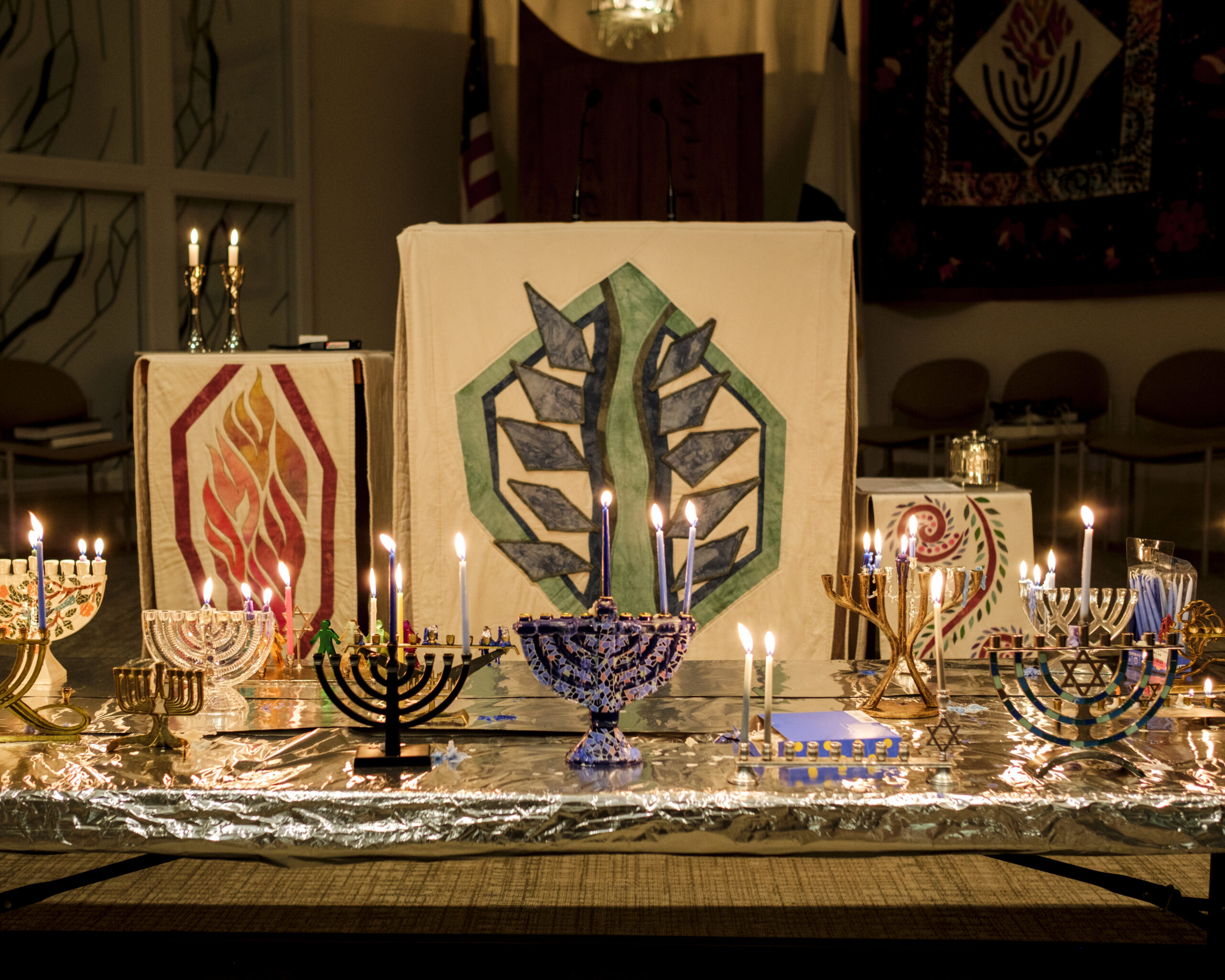 A table holds numerous menorahs with lighted candles
