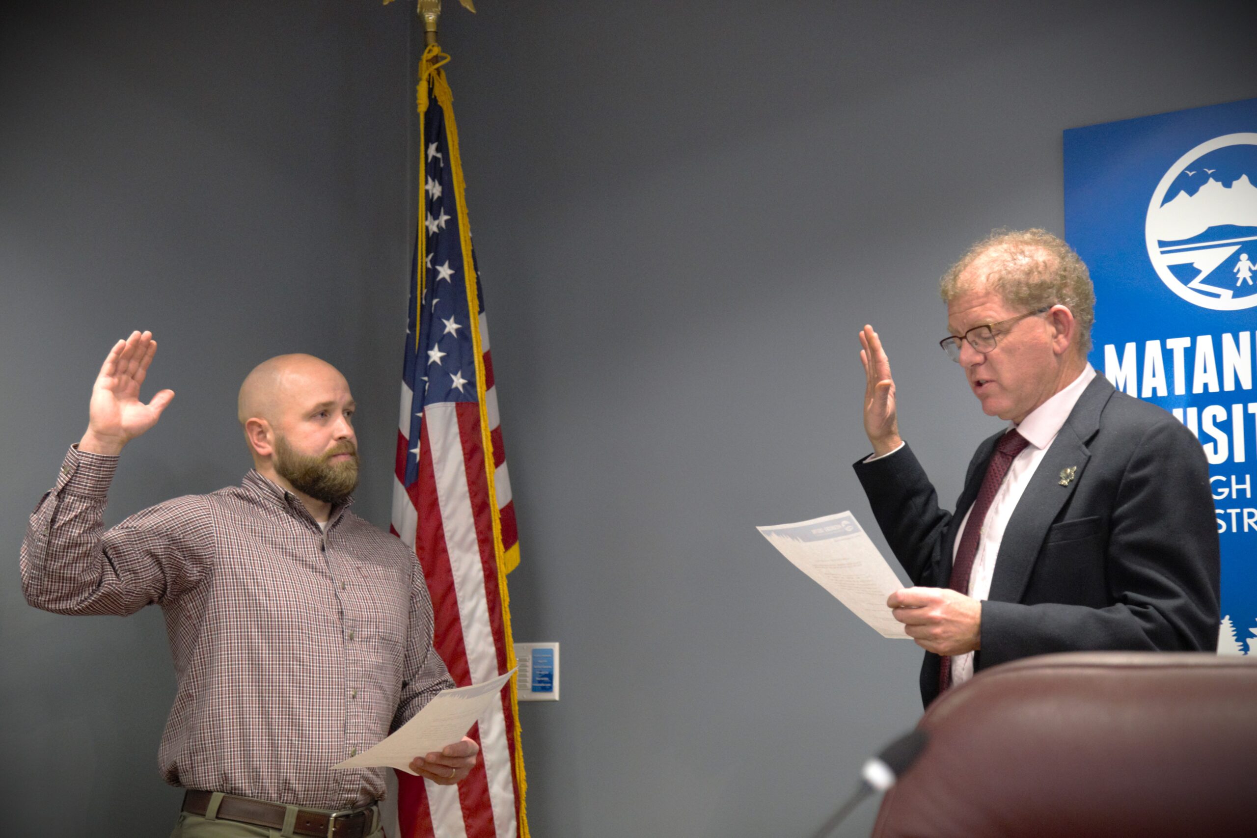 A man takes his oath of office in front of an American flag in the Mat-Su Borough School Board chambers.