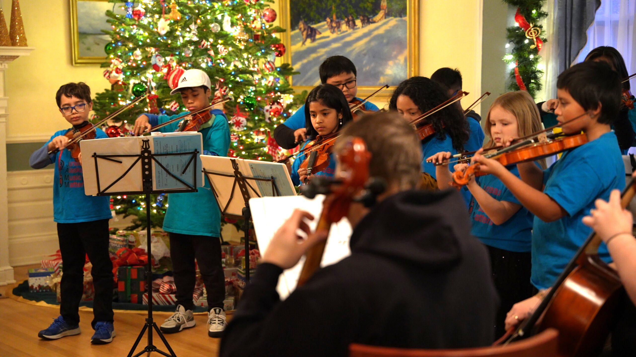 Children playing string instruments in front of Christmas tree
