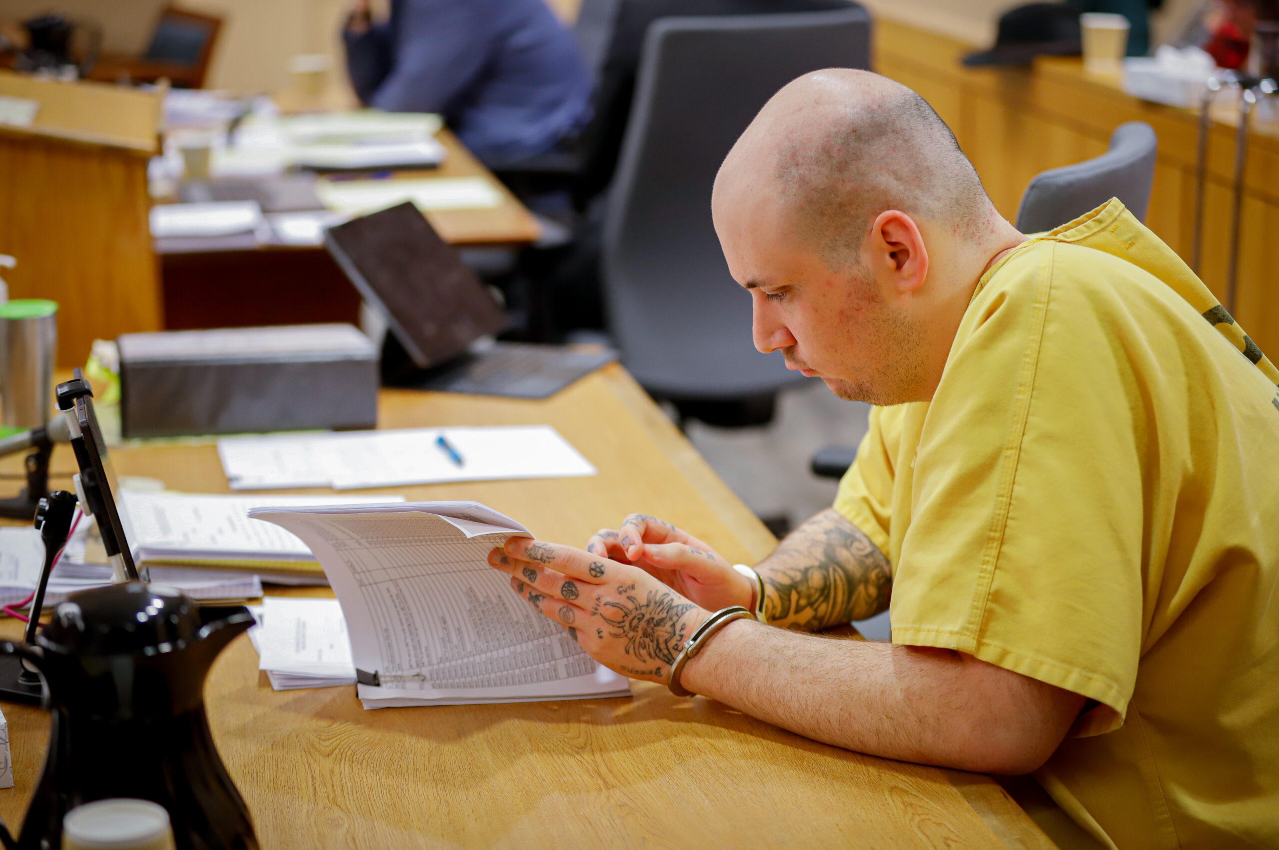 A man in a yellow prison jumper looks through documents