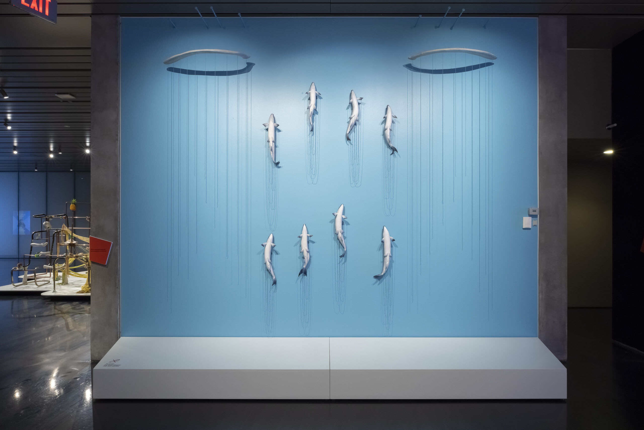 Eight carved basswood salmon are arranged to look like they are swimming up a blue wall. Blue beaded strands hang on either side of the fish.