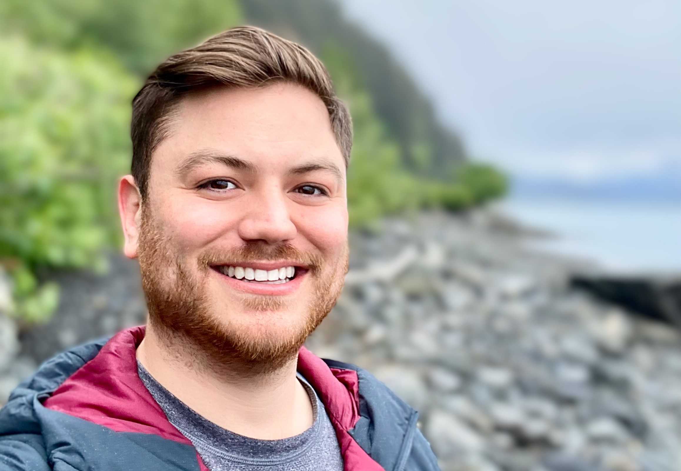 Man smiles with a beach and green hills in the background. 