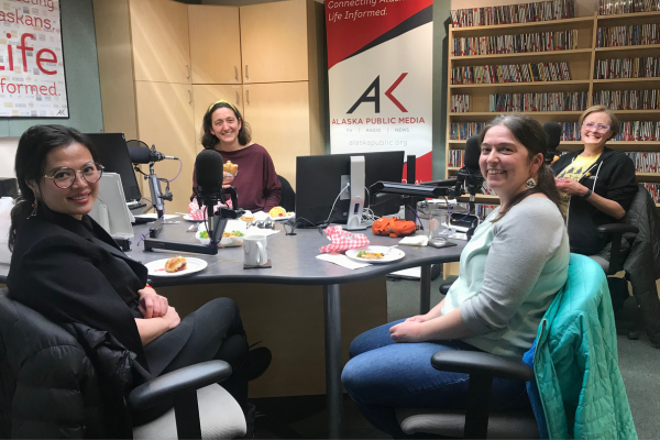 Four people sit around a radio table smiling and eating food.