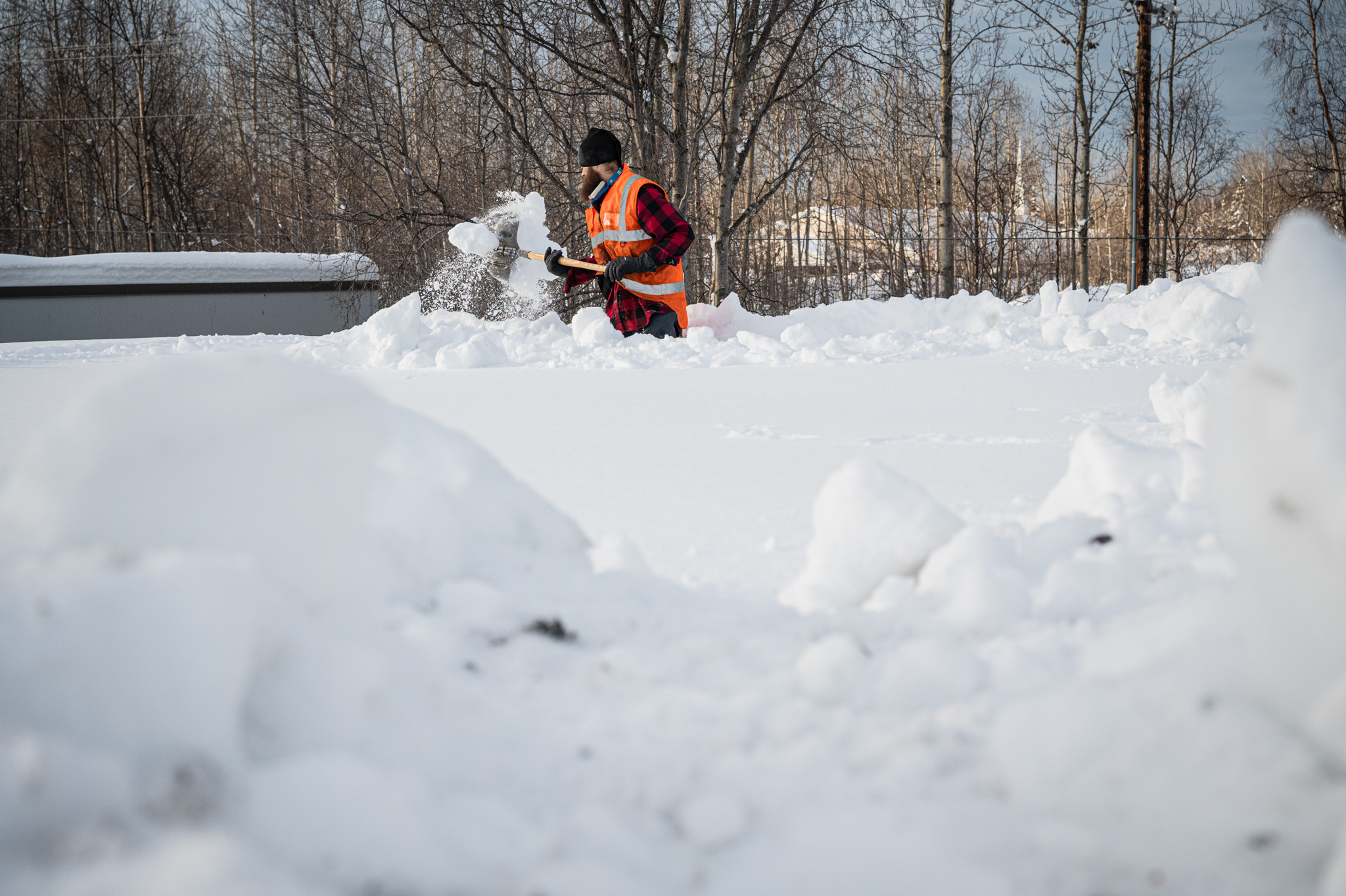 A man in a red plaid shirt shovels snow.