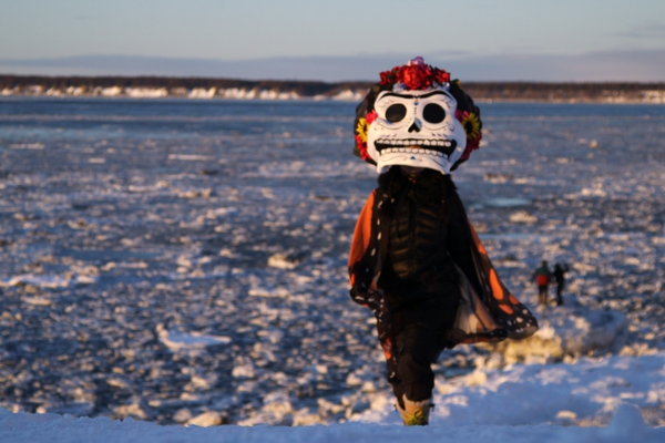 A person in a Day of the Dead mask walks on snow and ice. 