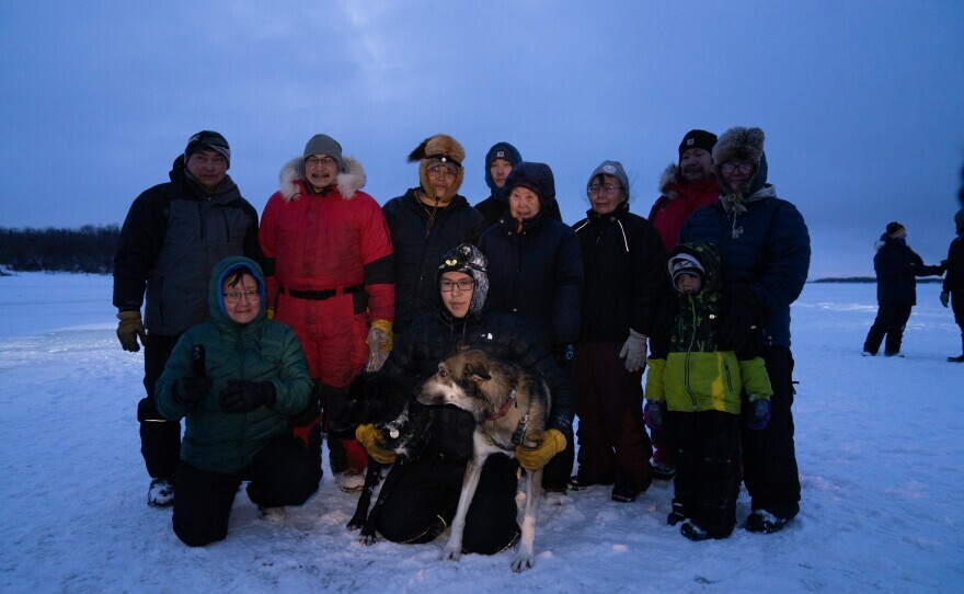 a group of people and a sled dog pose for a photo outside