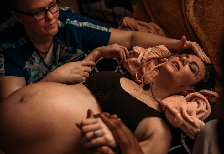 A midwife holds a pregnant mother's hand.