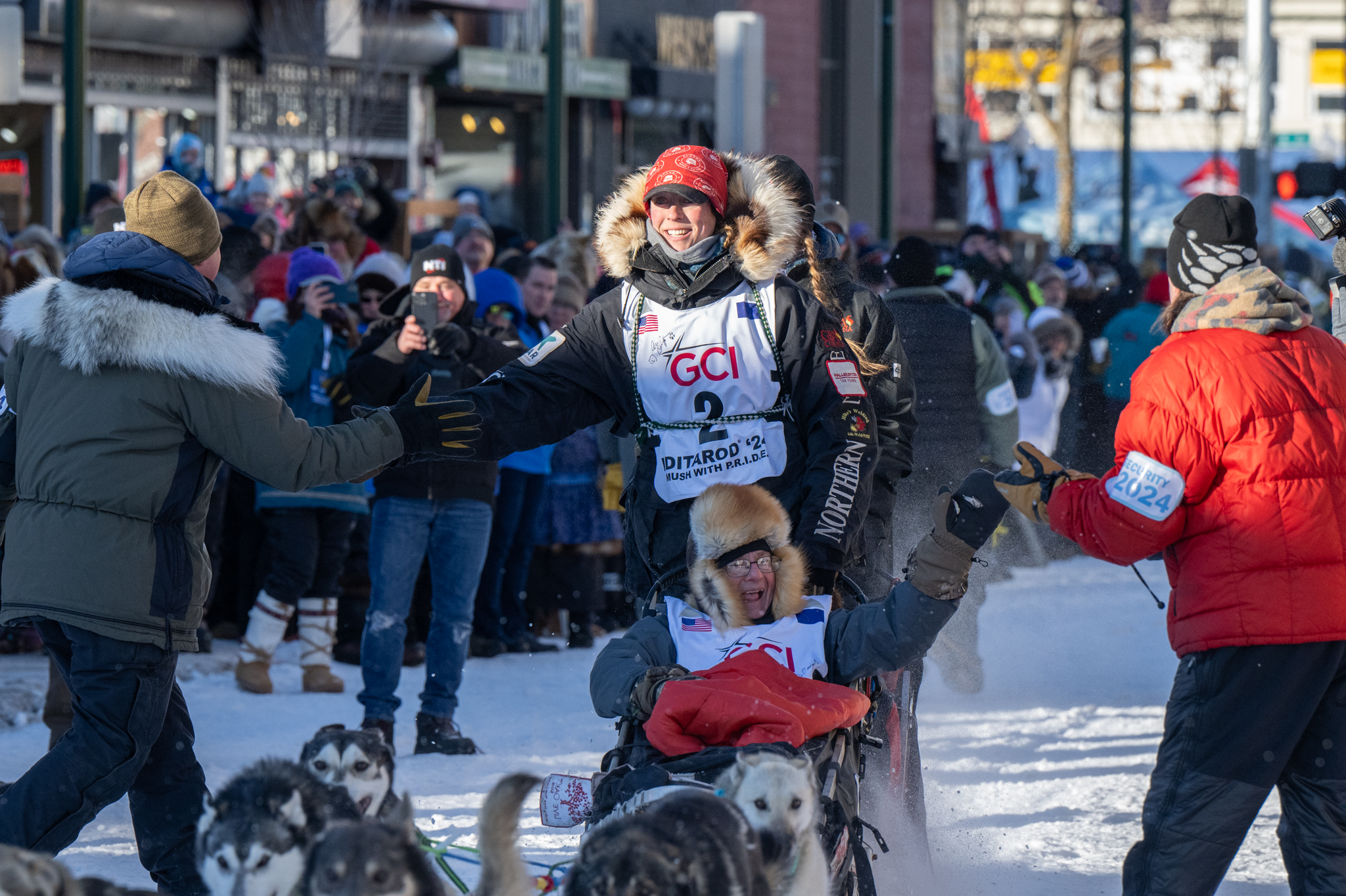 A woman in a sled dog shakes hands with a fan.