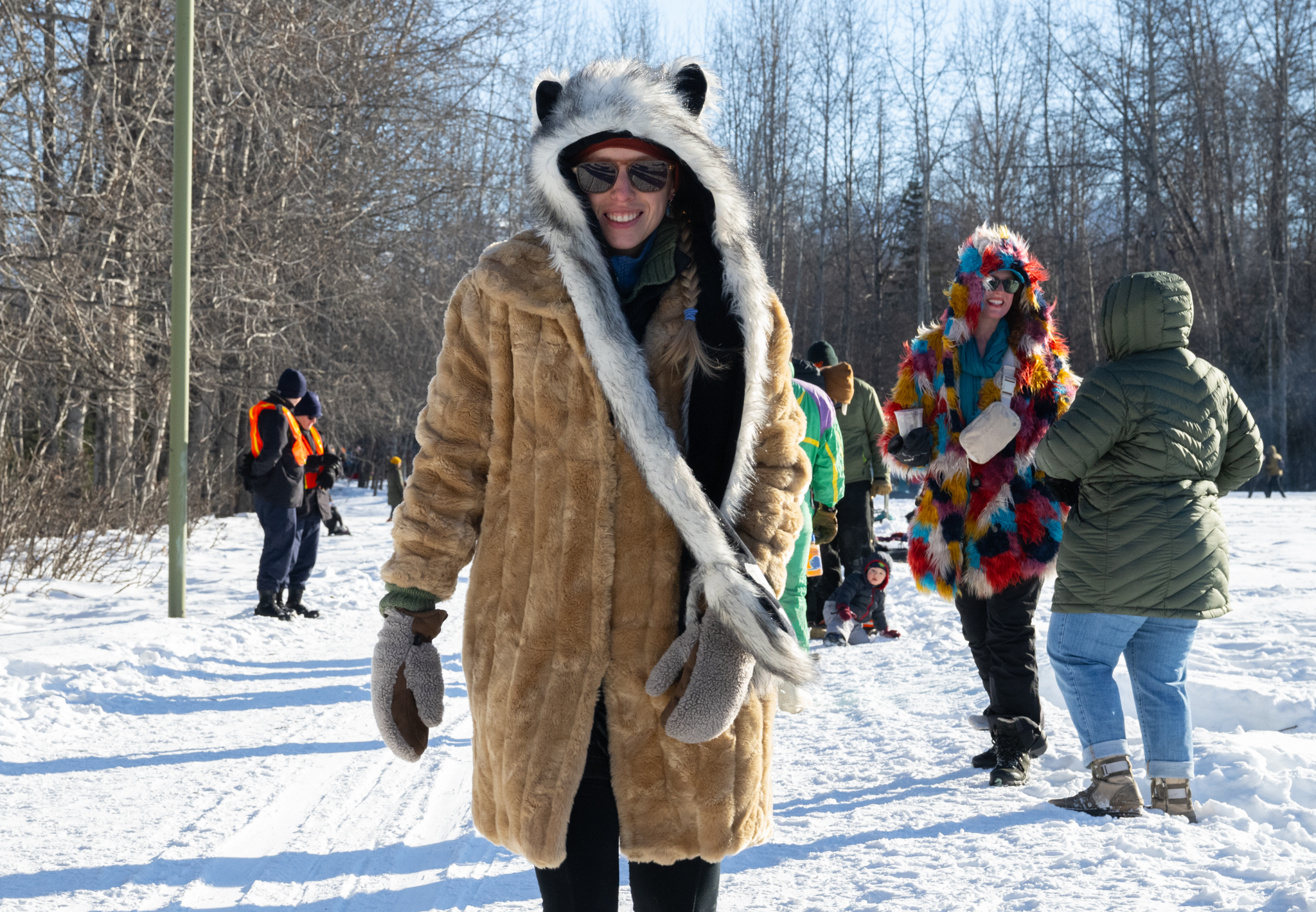 A woman wearing various furs walk on a winter trail.