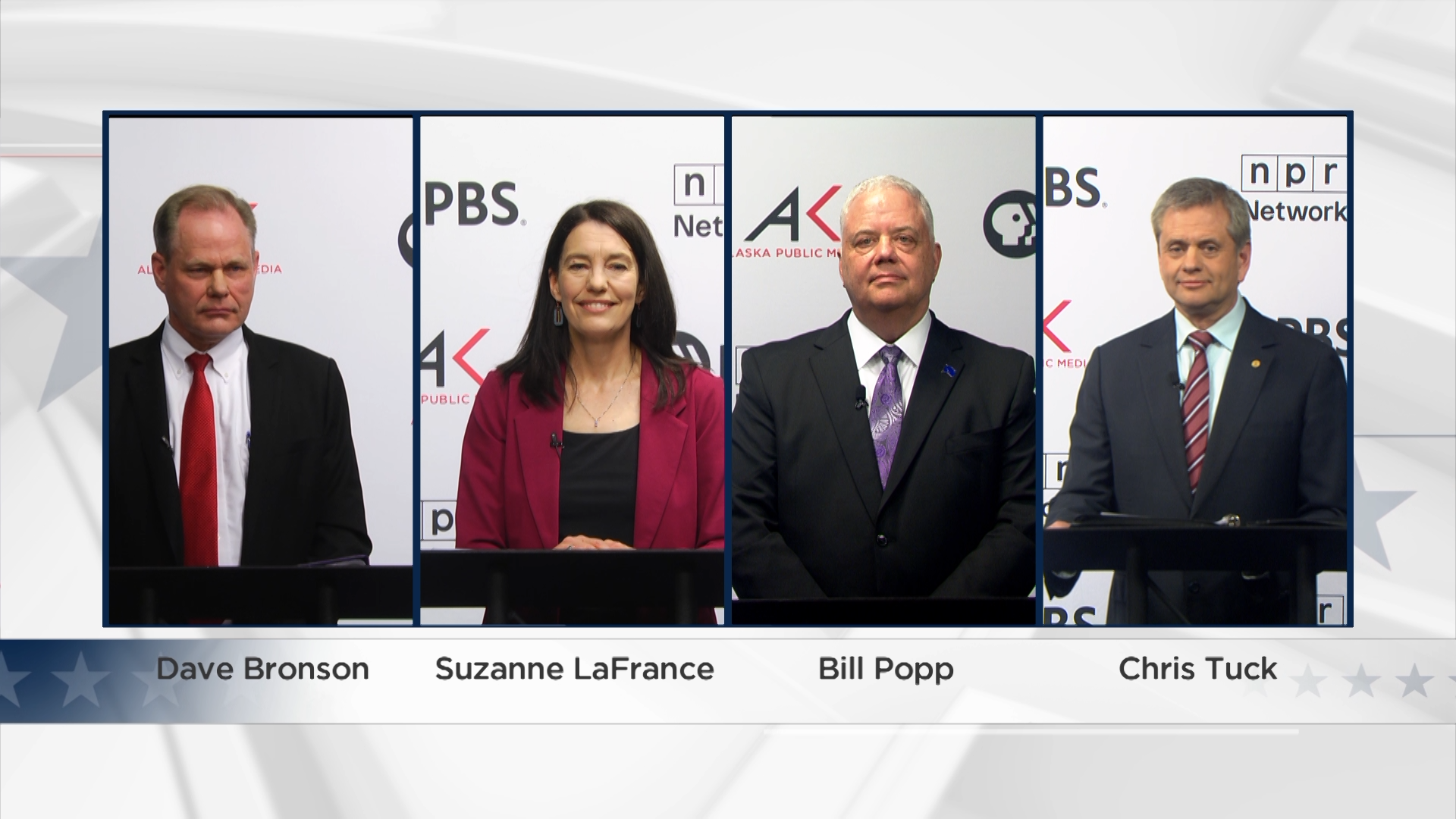 Four people, a man in a suit with red tie, a woman with a deep red blazer, a man in a suit with purple tie, and a man in a suit with a striped tie stand behind podiums in front of a white backdrop with the logos for PBS, NPR, and Alaska Public Media preparing for a debate.