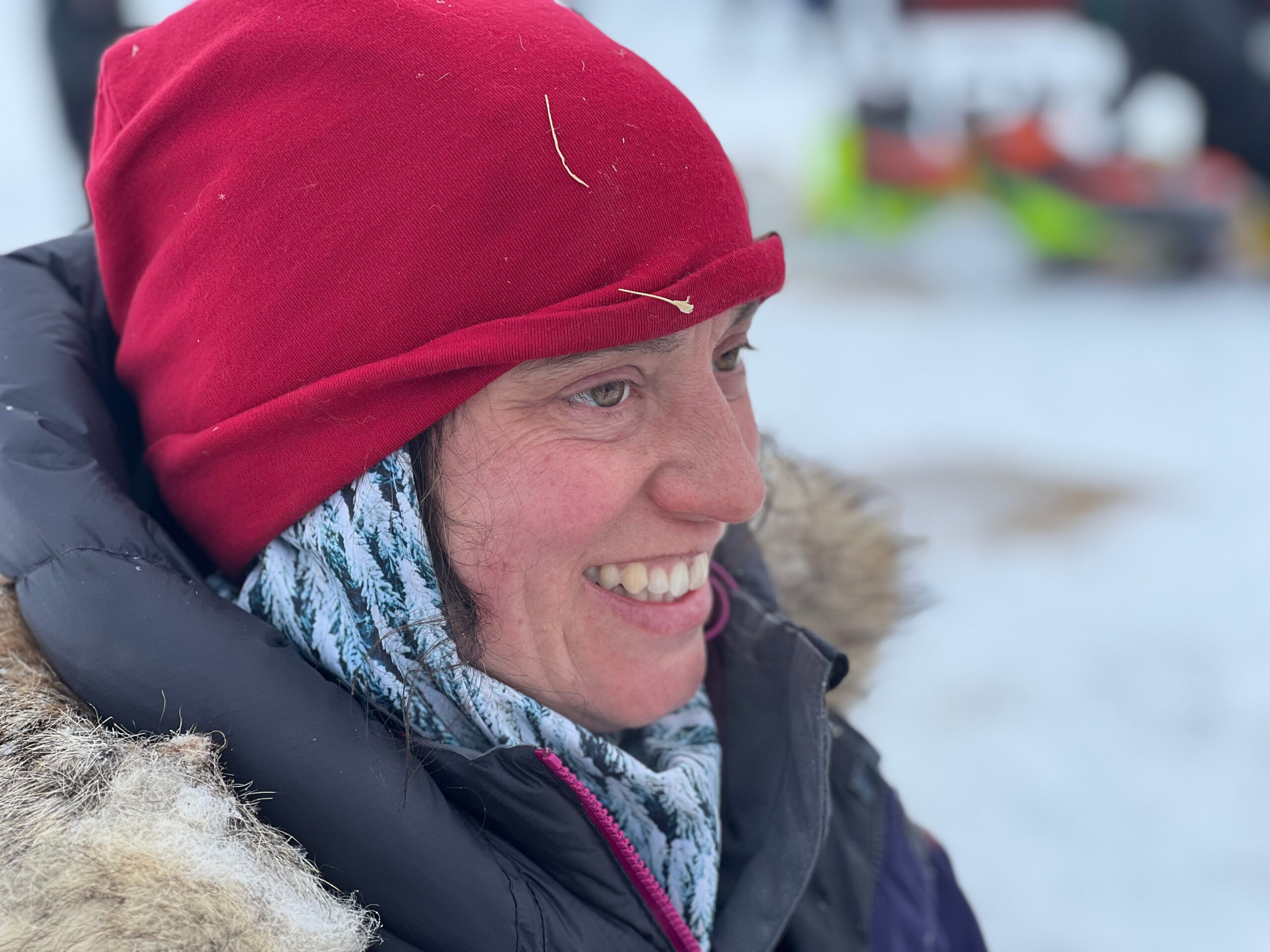 a smiling musher in a red hat