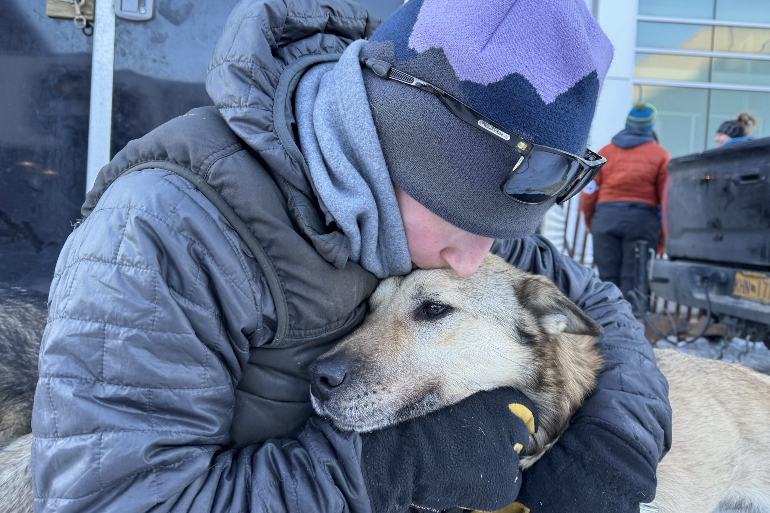 a musher kisses her dog on its head