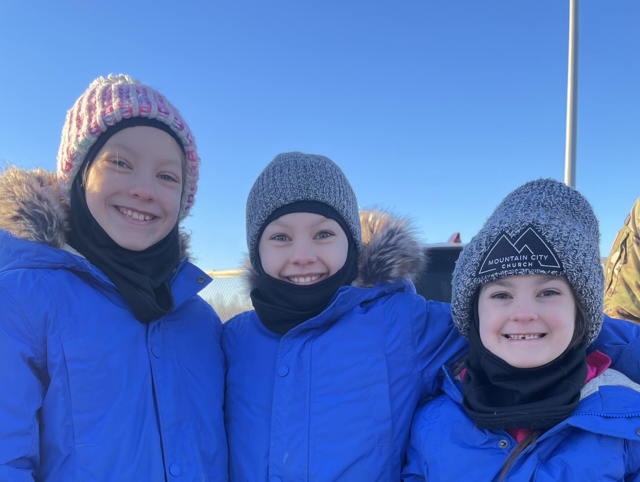 Three sisters smile in their warm winter gear.