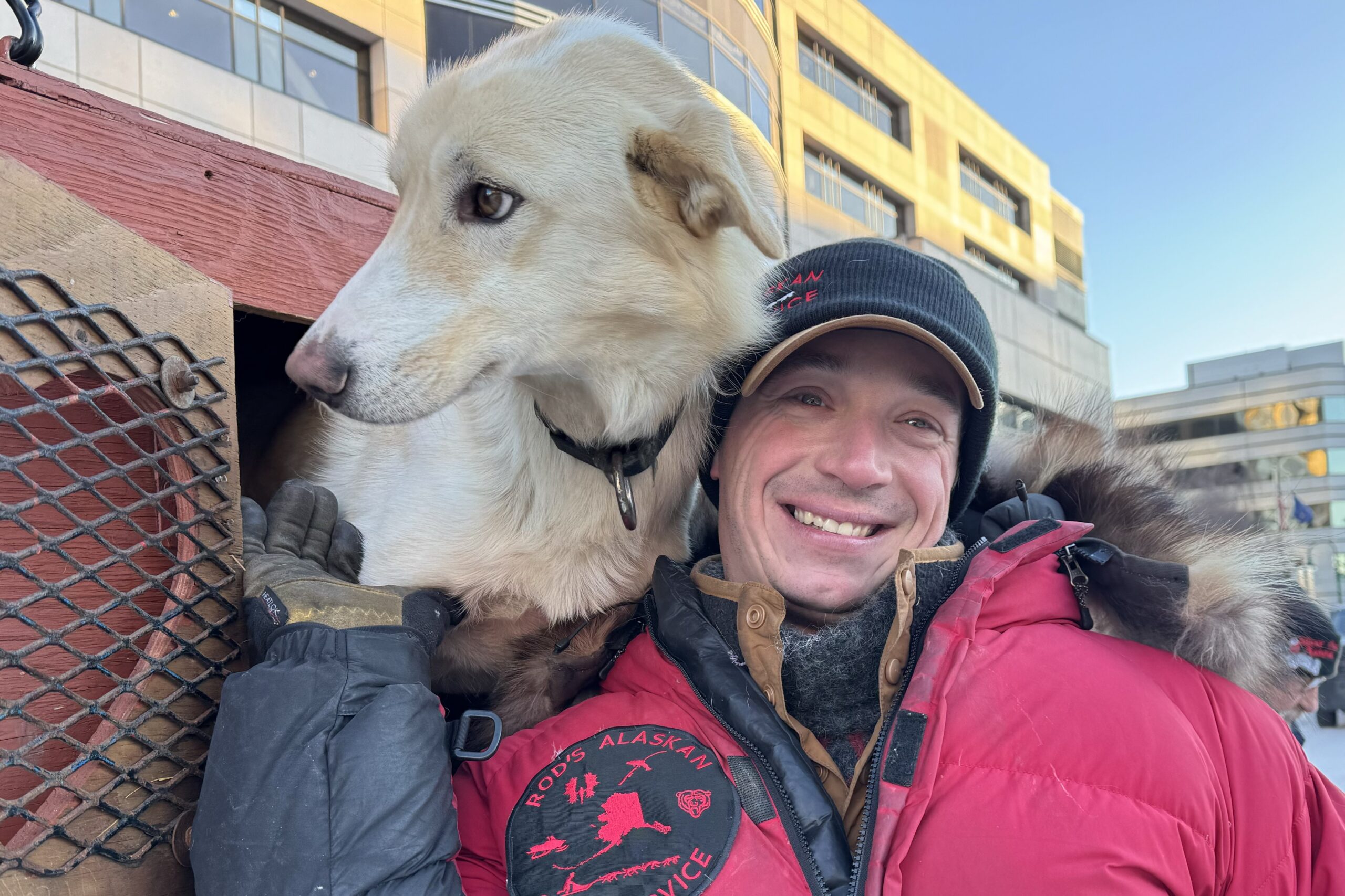 a musher poses with a blonde dog outside