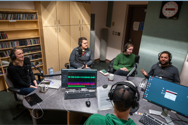 People sit around a radio studio table.
