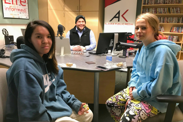 Two teen girls and an adult man sit at a radio studio table.